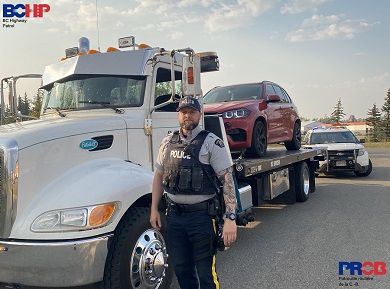 BC Highway Patrol officer next to a tow truck towing a red BMW 